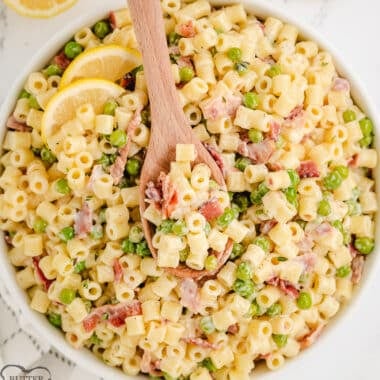 creamy bacon pasta salad in a white bowl with a wooden spoon