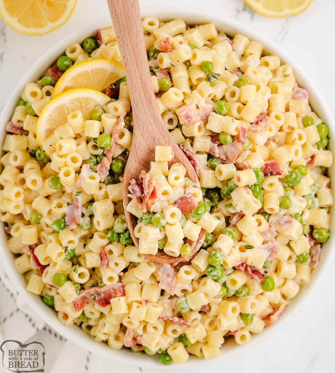 creamy bacon pasta salad in a white bowl with a wooden spoon