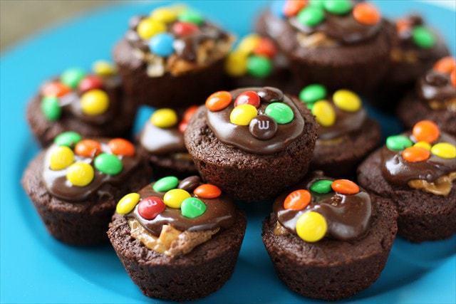 Snickers Brownie Bites made from homemade brownie recipe then stuffed with Snickers bites and topped with chocolate frosting and chocolate candies. 