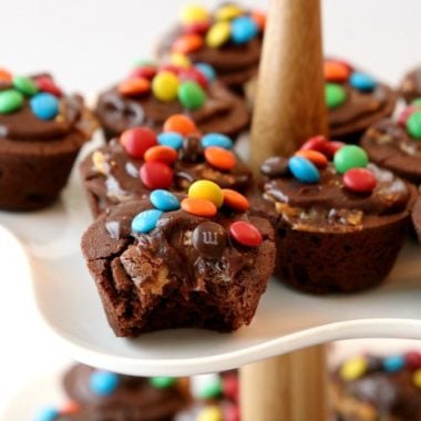 Snickers Brownie Bites made from a homemade brownie recipe then stuffed with Snickers candy and topped with chocolate frosting and chocolate candies.