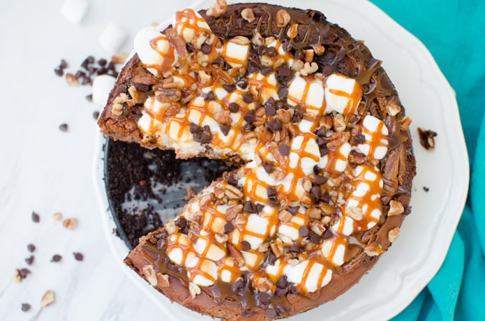 Rocky Road Cheesecake is a chocolate cheesecake with marshmallows, pecans, chocolate chips, and caramel.