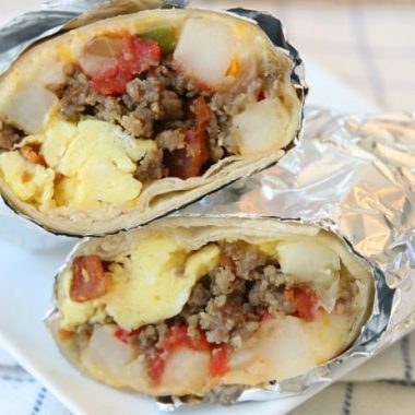 Loaded Breakfast Burrito recipe made with eggs, tomatoes, cheese, hash browns, sausage, bacon and more! Cook and assemble, then eat for breakfast or dinner and freeze the rest!