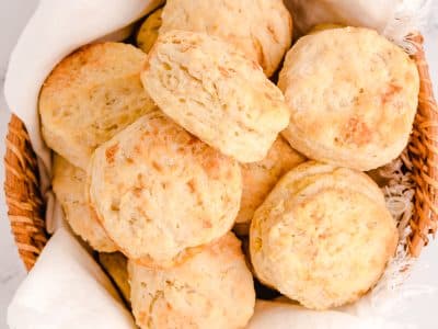 buttery flaky homemade biscuits in a basket with a white cloth