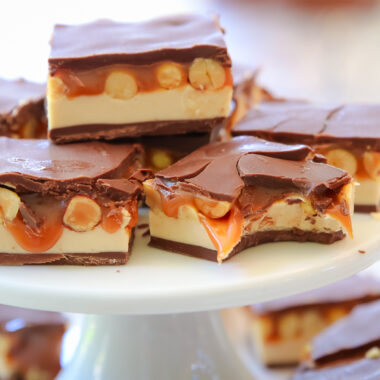 gooey homemade snickers bars on a white plate, one has a bite taken out
