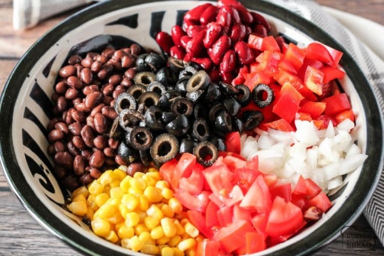 beans, tomatoes, onions, olives, corn and peppers in a bowl to make taco salad