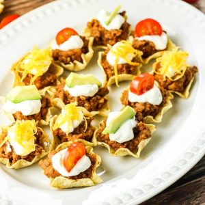 Taco Bites are tortilla chips filled with a combination of ground beef, refried beans and taco seasoning topped off with your favorite toppings. These mini taco bites are perfect to serve as an appetizer or a fun family meal.