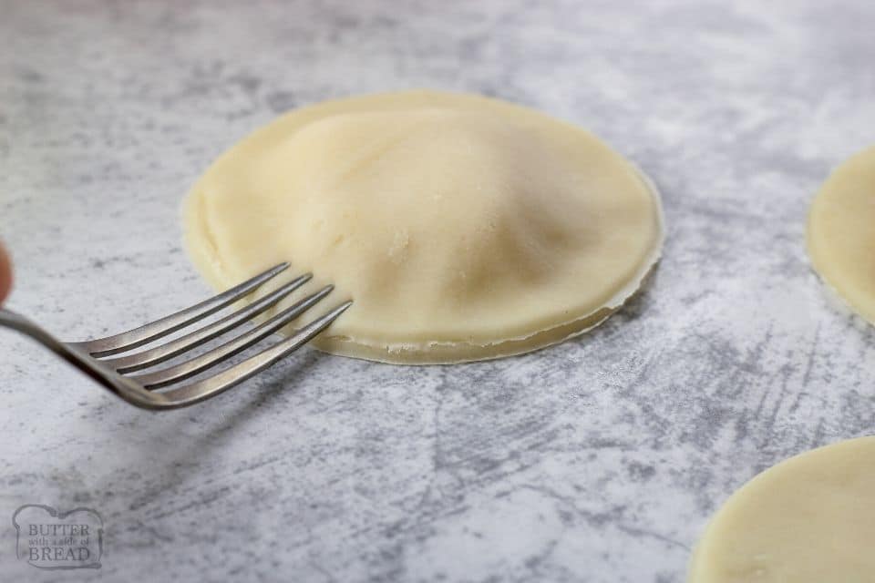 using a fork to press pie crust together around a mini pie