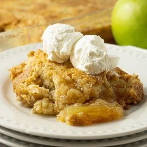 apple dump cake on stacked white plates with whipped cream