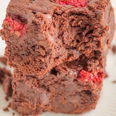 two squares of thick raspberry chocolate brownies stacked with a bite taken out of one