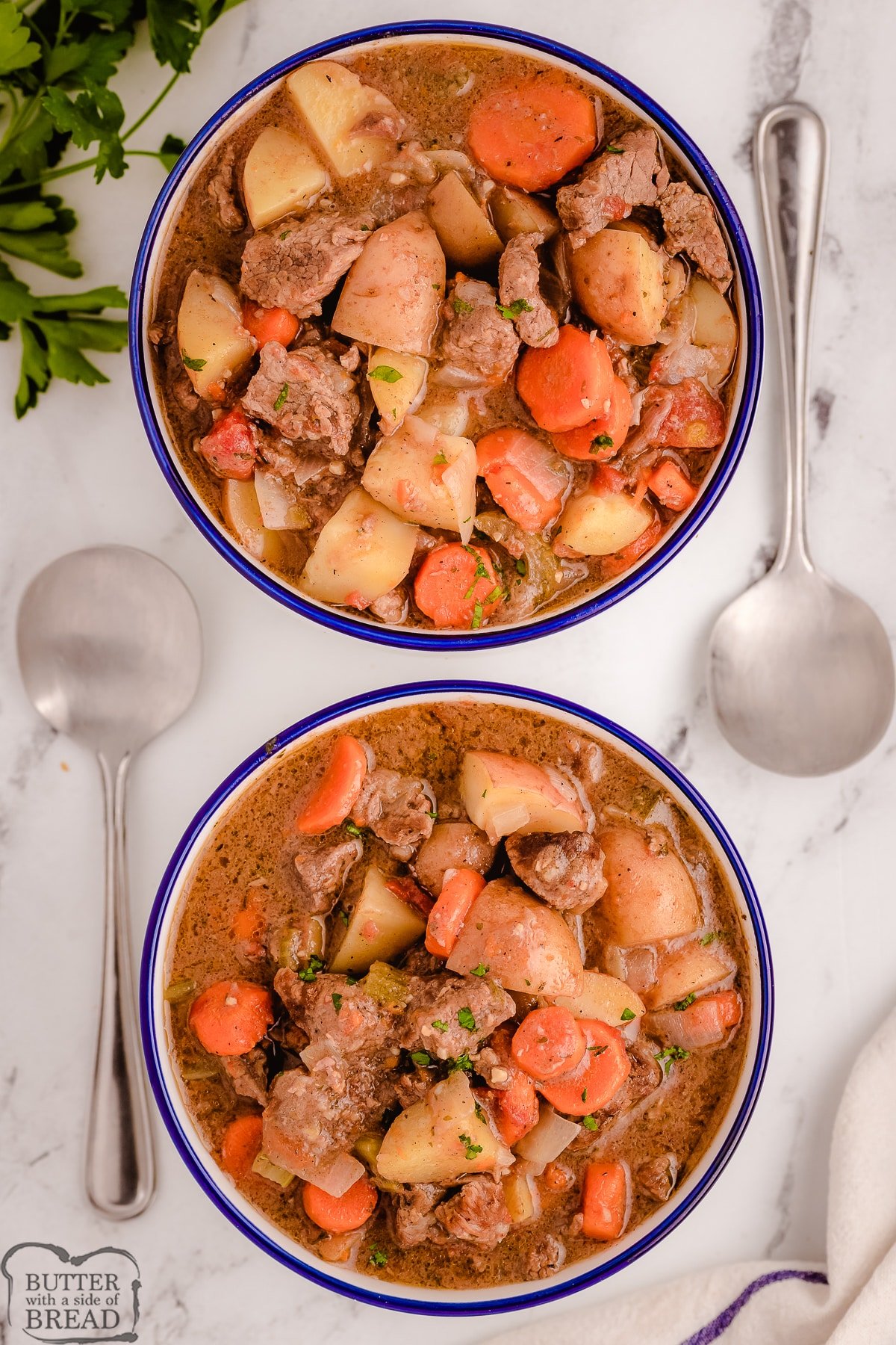 two bowls of crockpot beef stew with large spoons