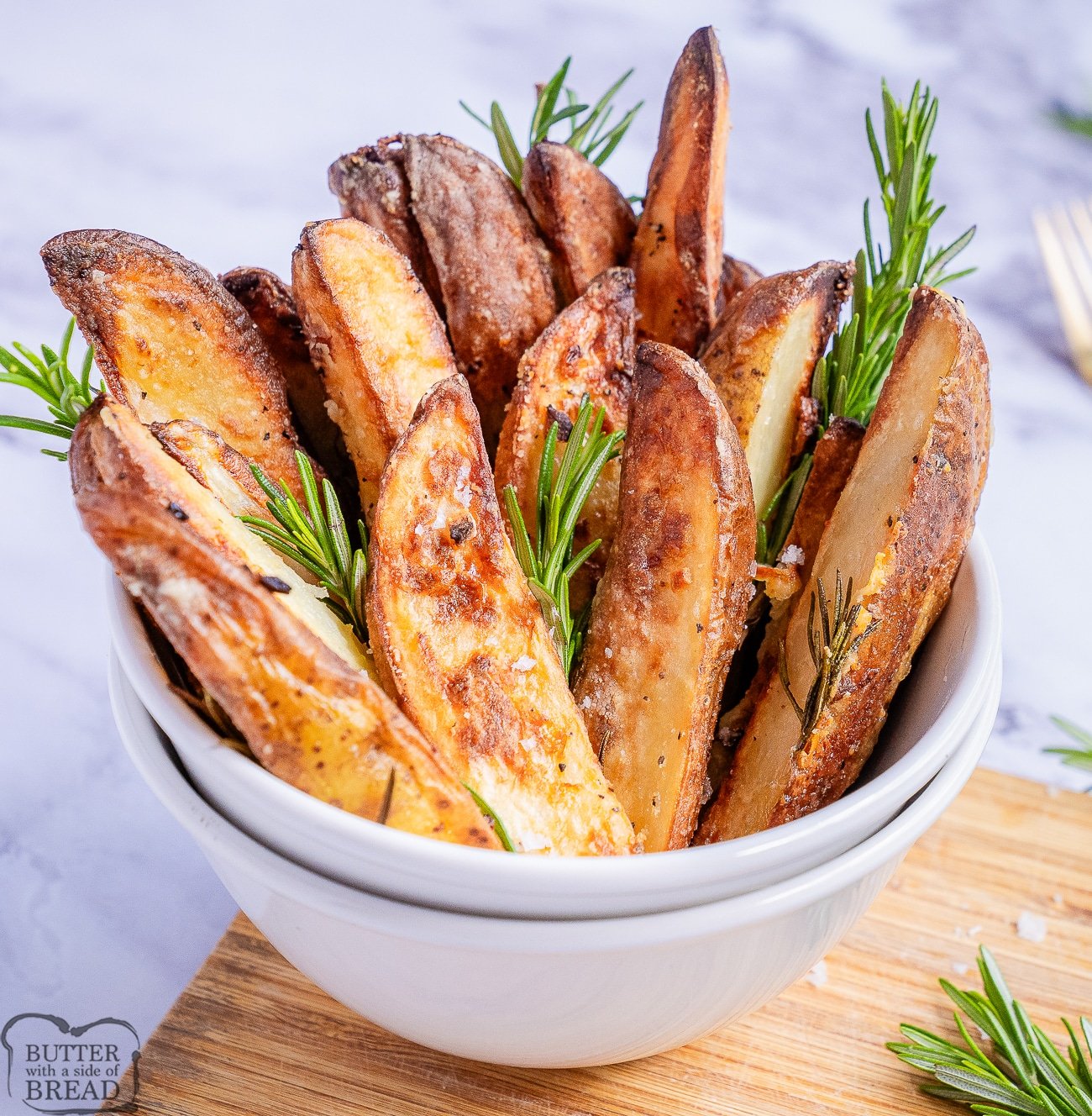 crispy roasted rosemary potato wedges in a bowl with fresh rosemary