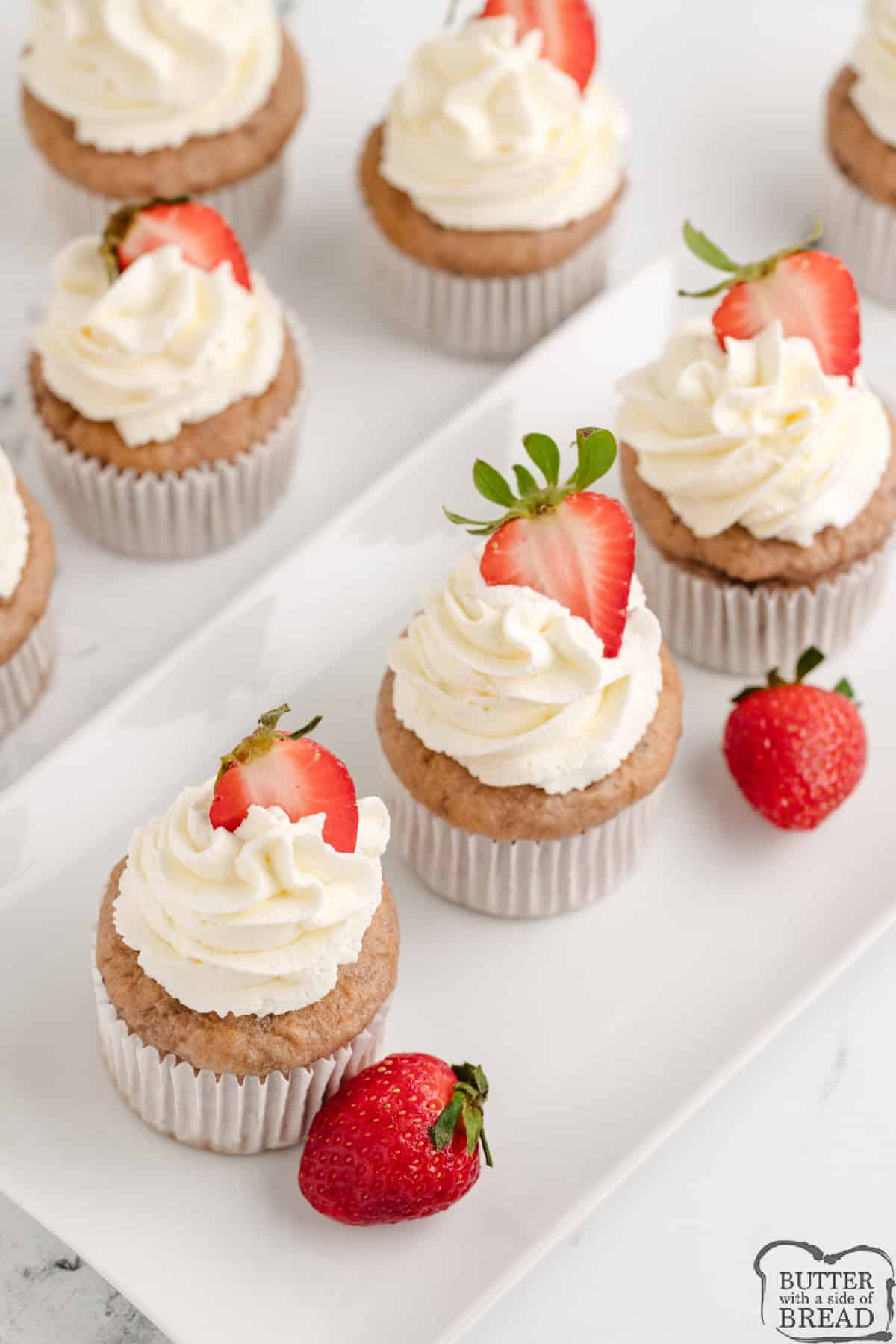 Cupcakes topped with whipped cream and strawberries. 