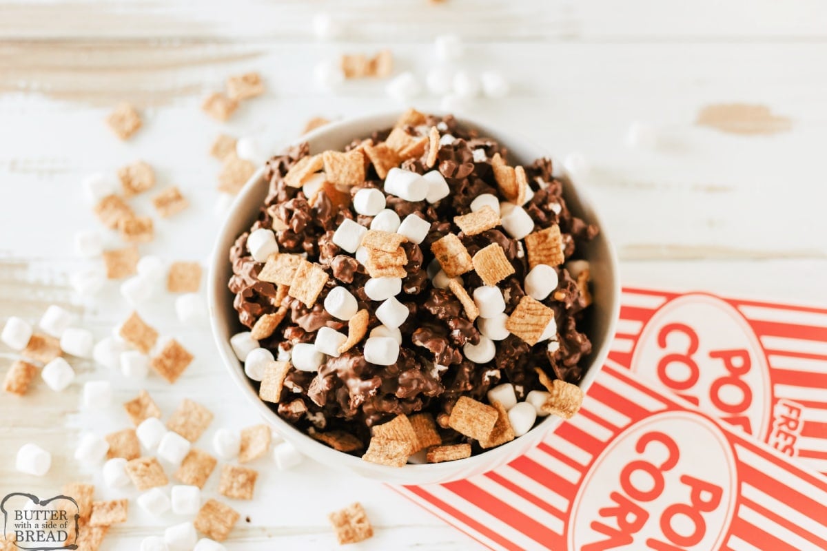 Adding cereal and marshmallows to chocolate coated popcorn. 
