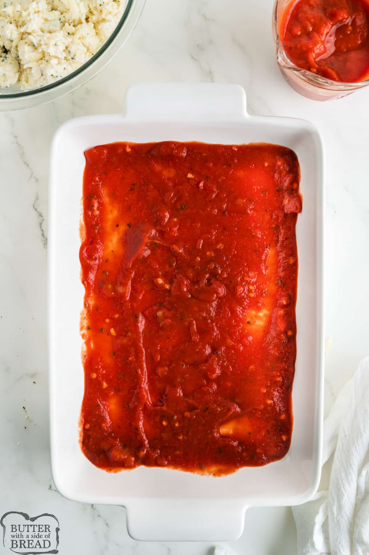 Spreading marinara sauce on the bottom of the pan.