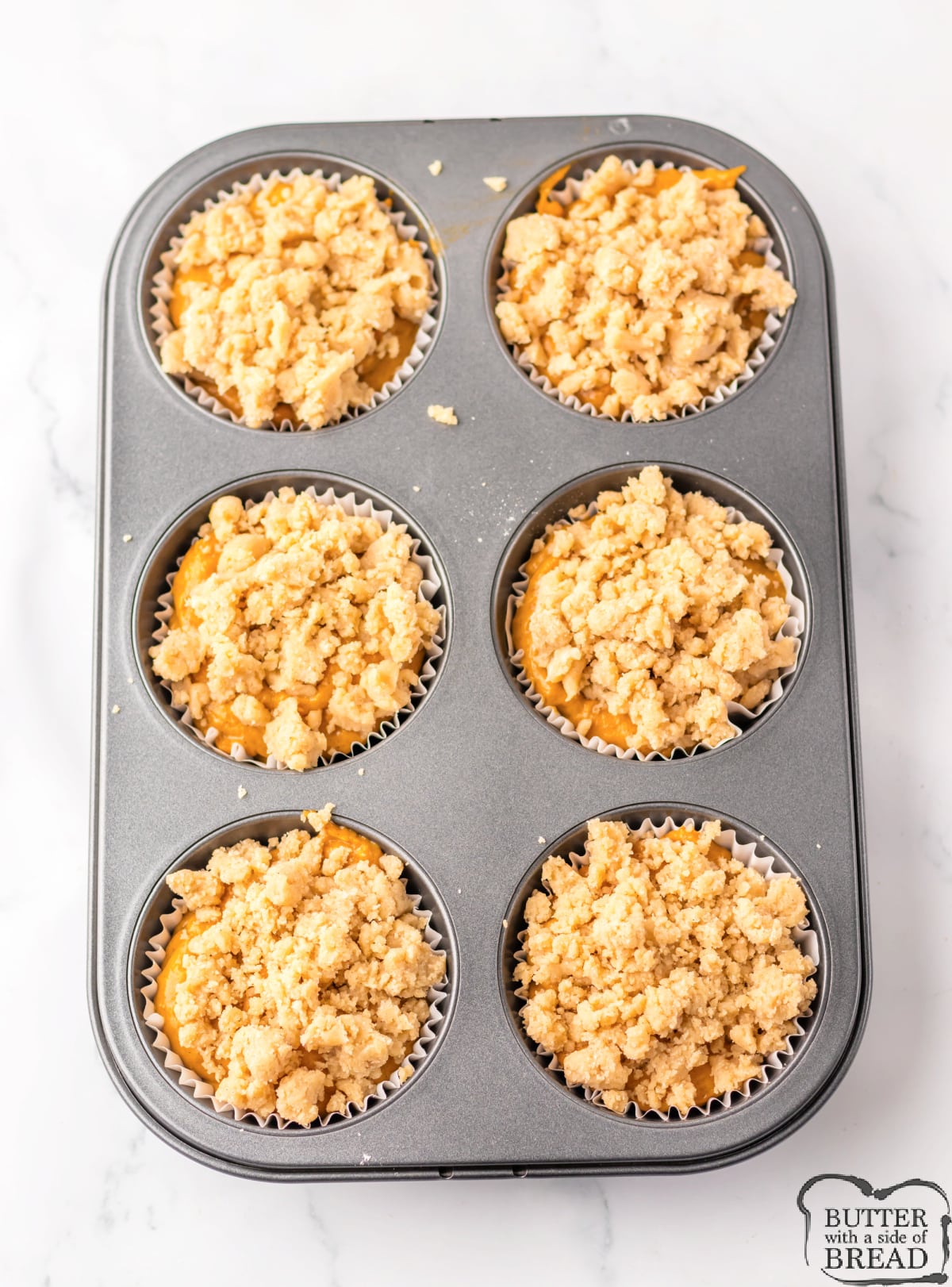 Sprinkling crumb topping over muffin batter. 