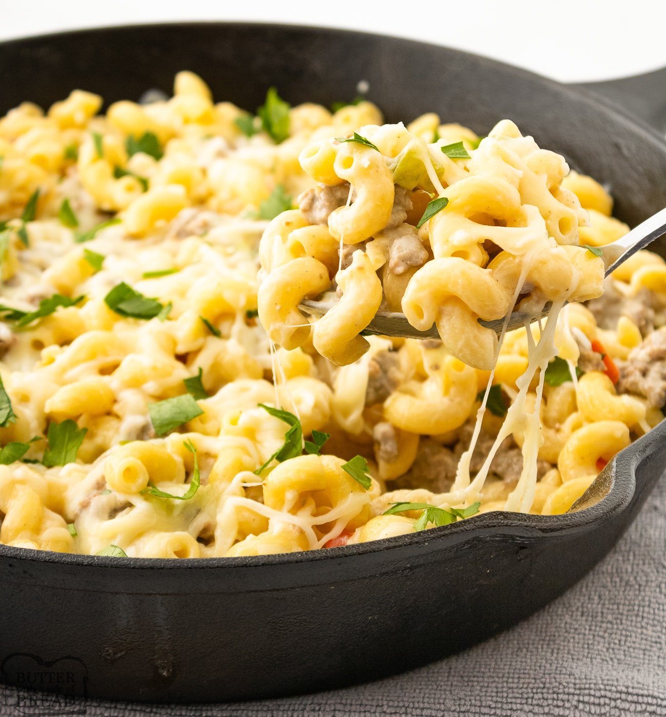 scooping Philly Cheesesteak pasta from a cast iron skillet for dinner