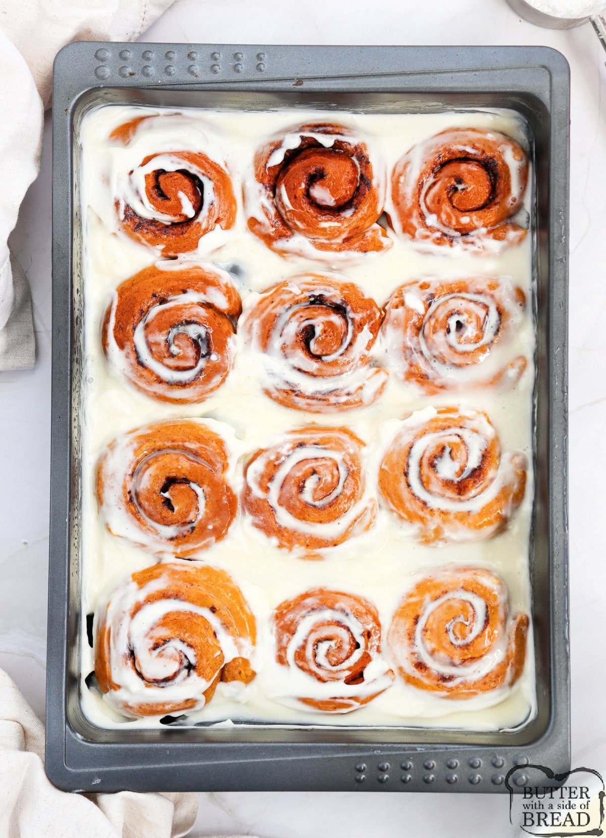 Spreading cream cheese frosting over baked cinnamon rolls. 