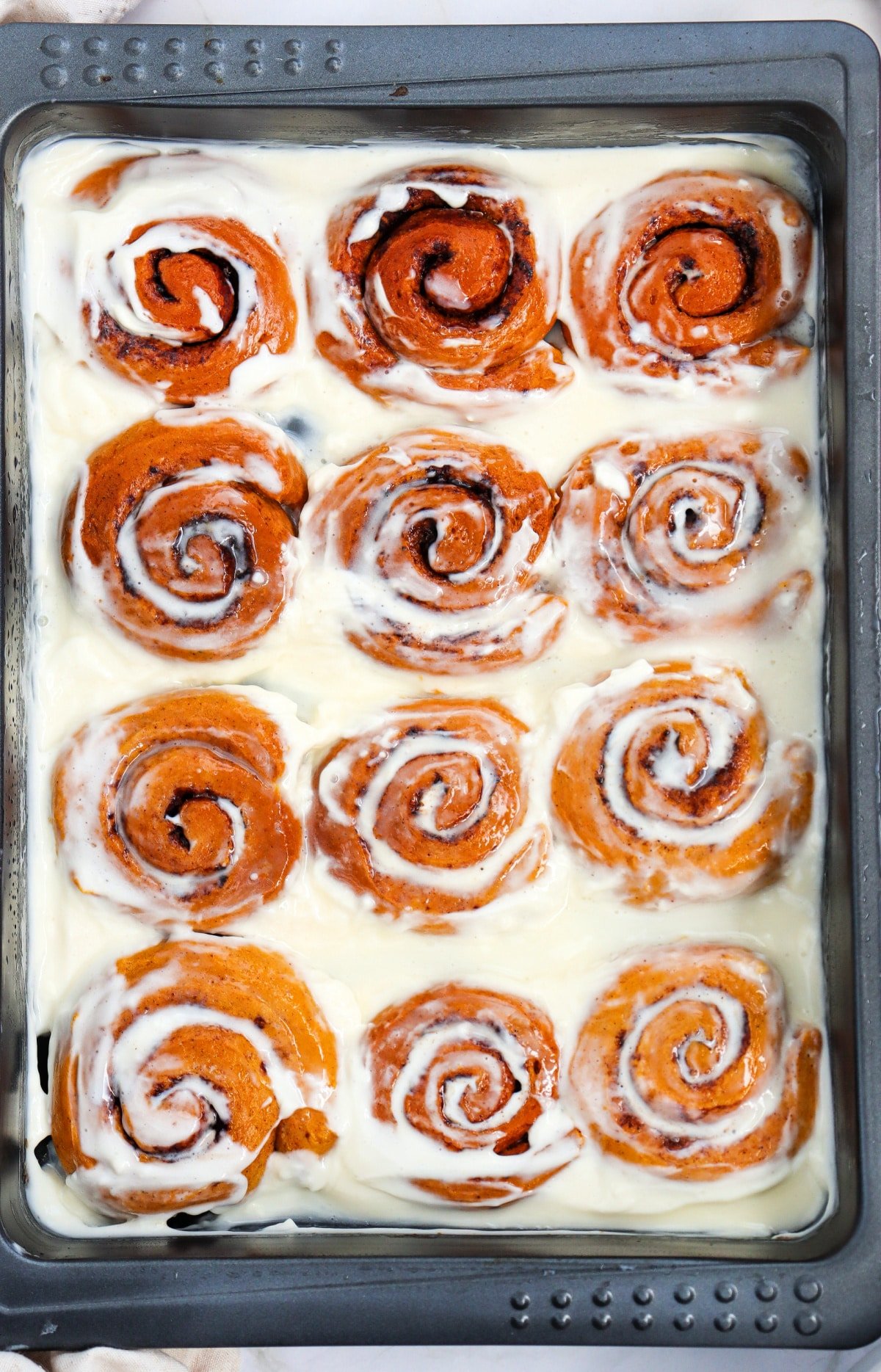 Pan of pumpkin cinnamon rolls frosted with cream cheese frosting.