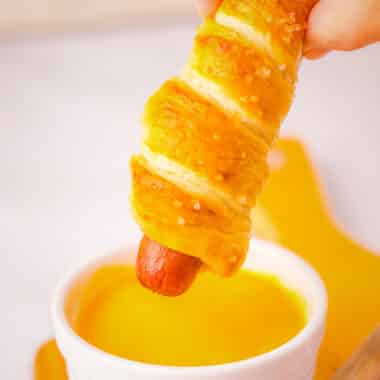 dipping a pretzel hot dog in cheese sauce