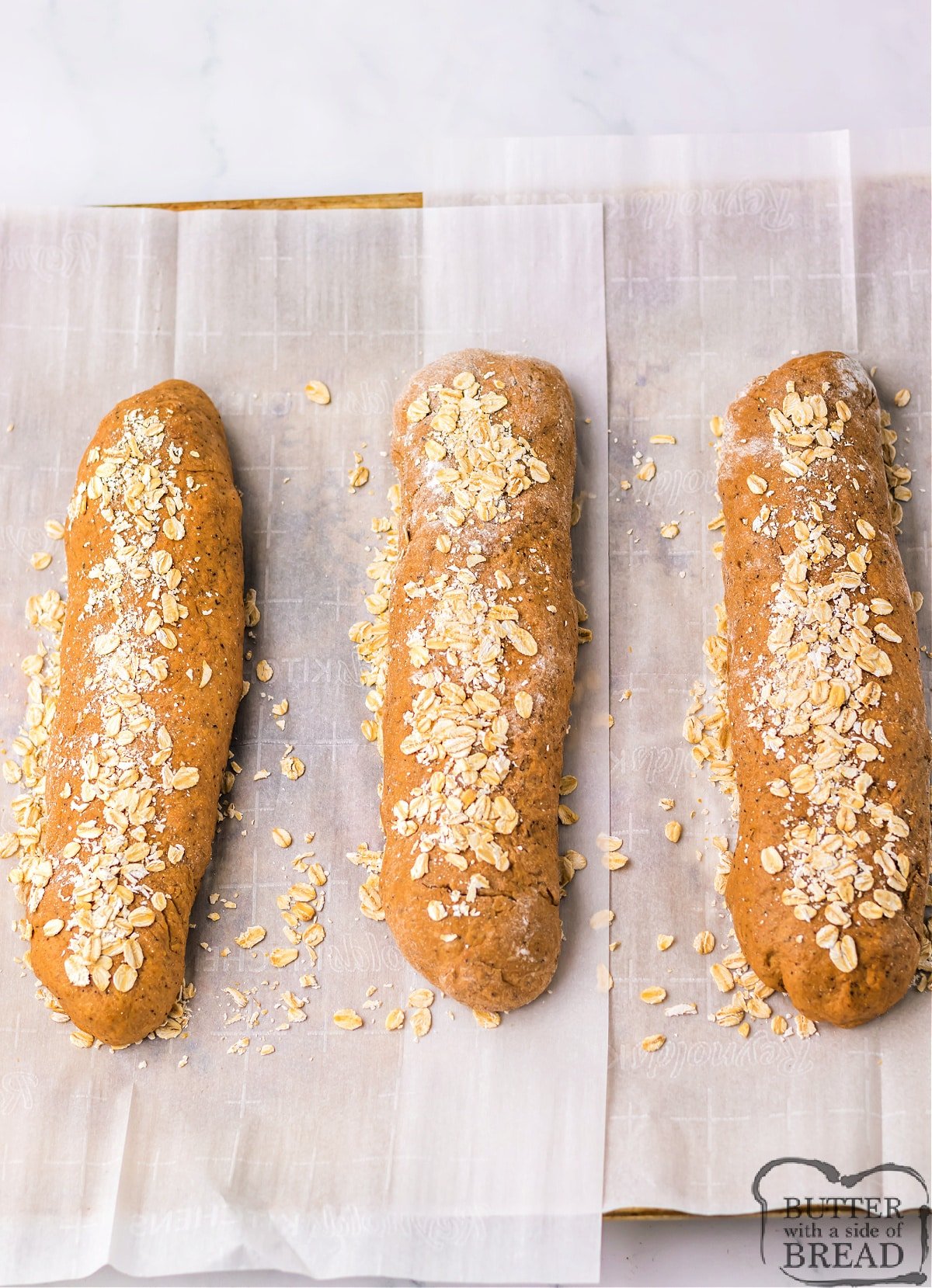 Three loaves of shaped bread with oats on top. 