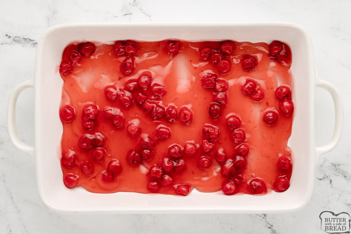 Placing cherry pie filling in the bottom of a casserole dish.