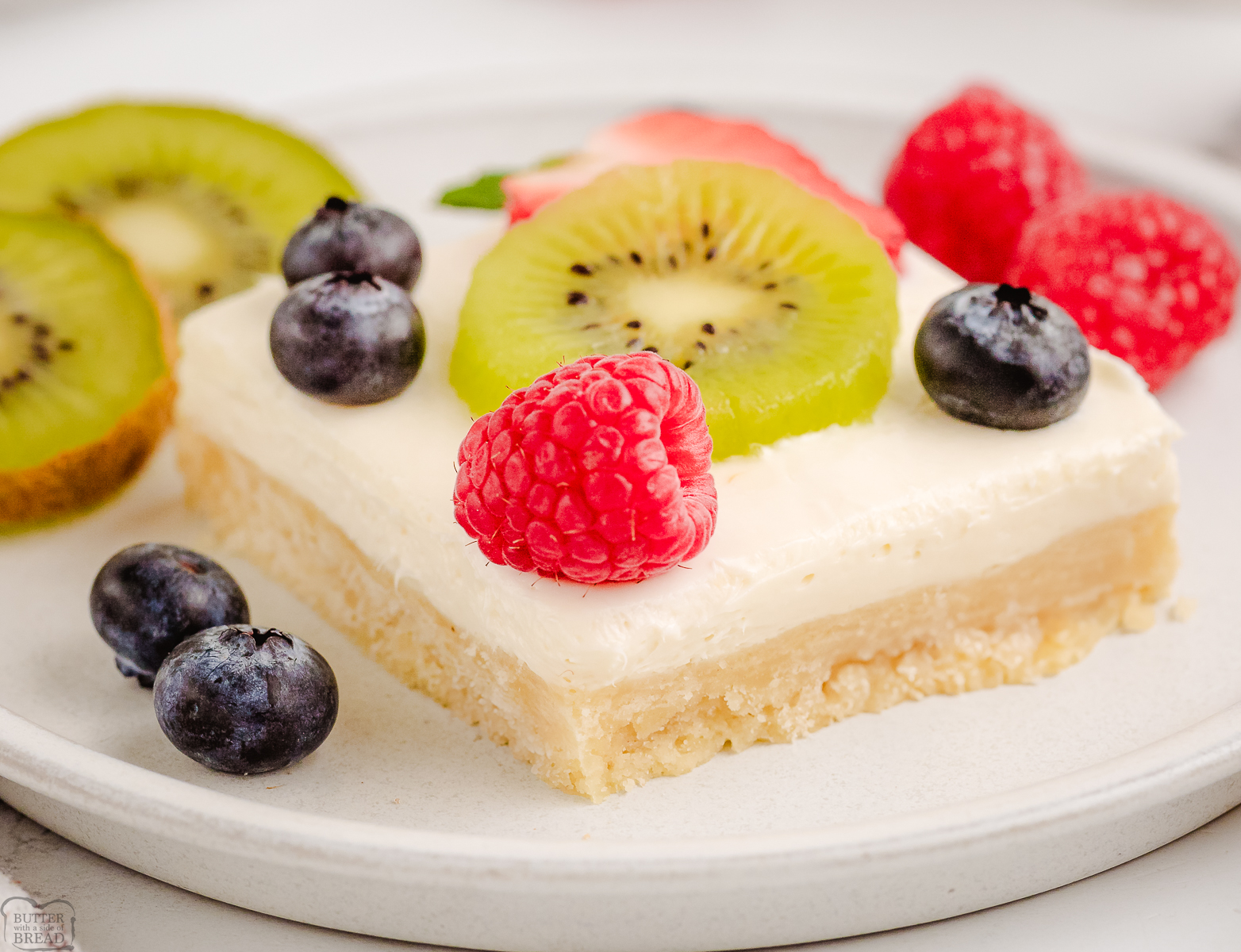 layered shortbread topped with cheesecake filling and berries with kiwi fruit