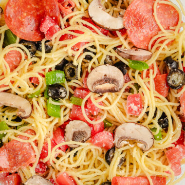 big bowl of angel hair pasta with pepperoni, olives and cheese