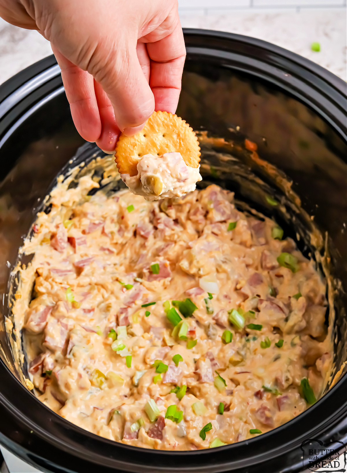 A Ritz cracker dipped in warm cheesy sausage dip in a slow cooker.