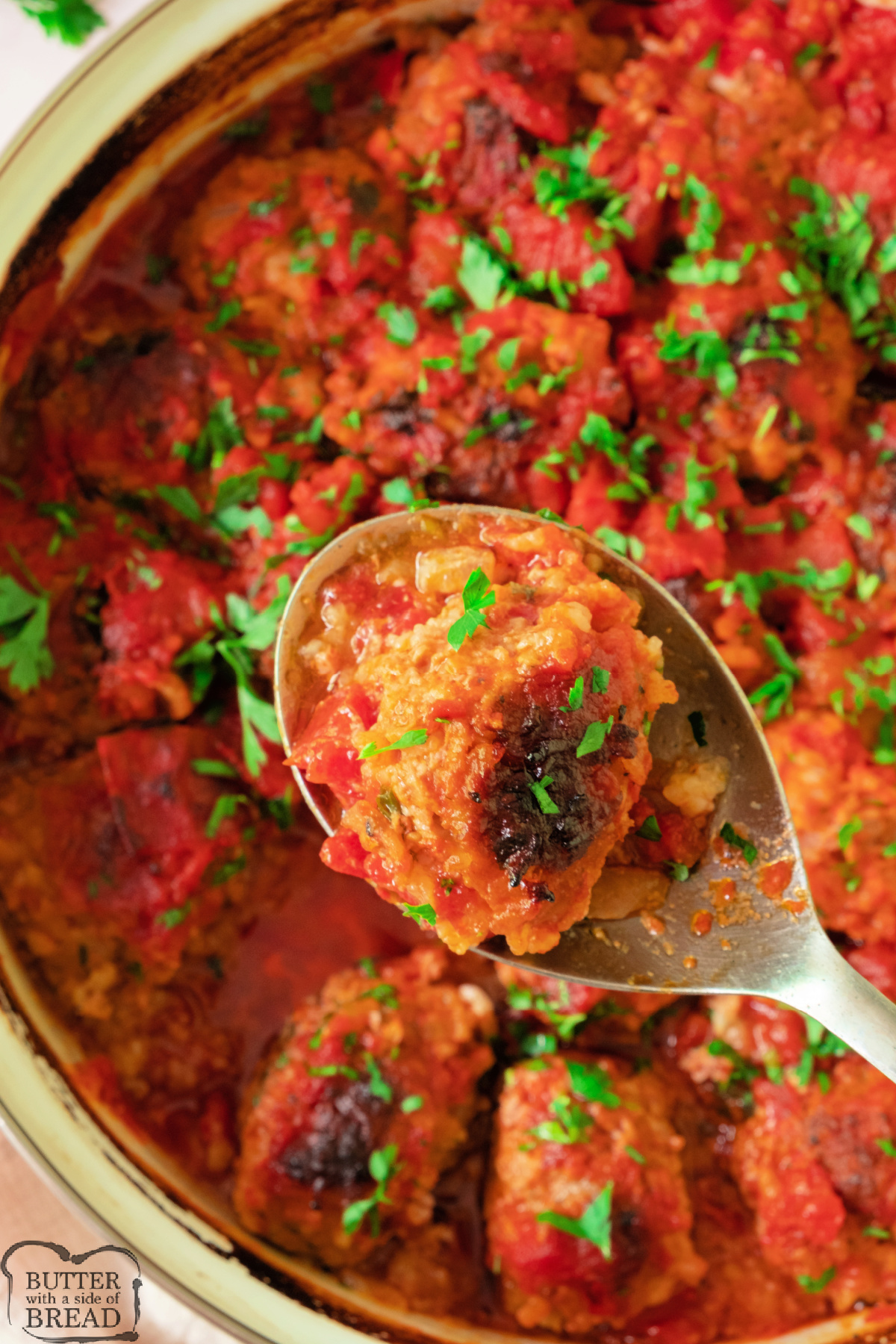 Spoon lifting a porcupine meatball out of a saucy casserole dish.
