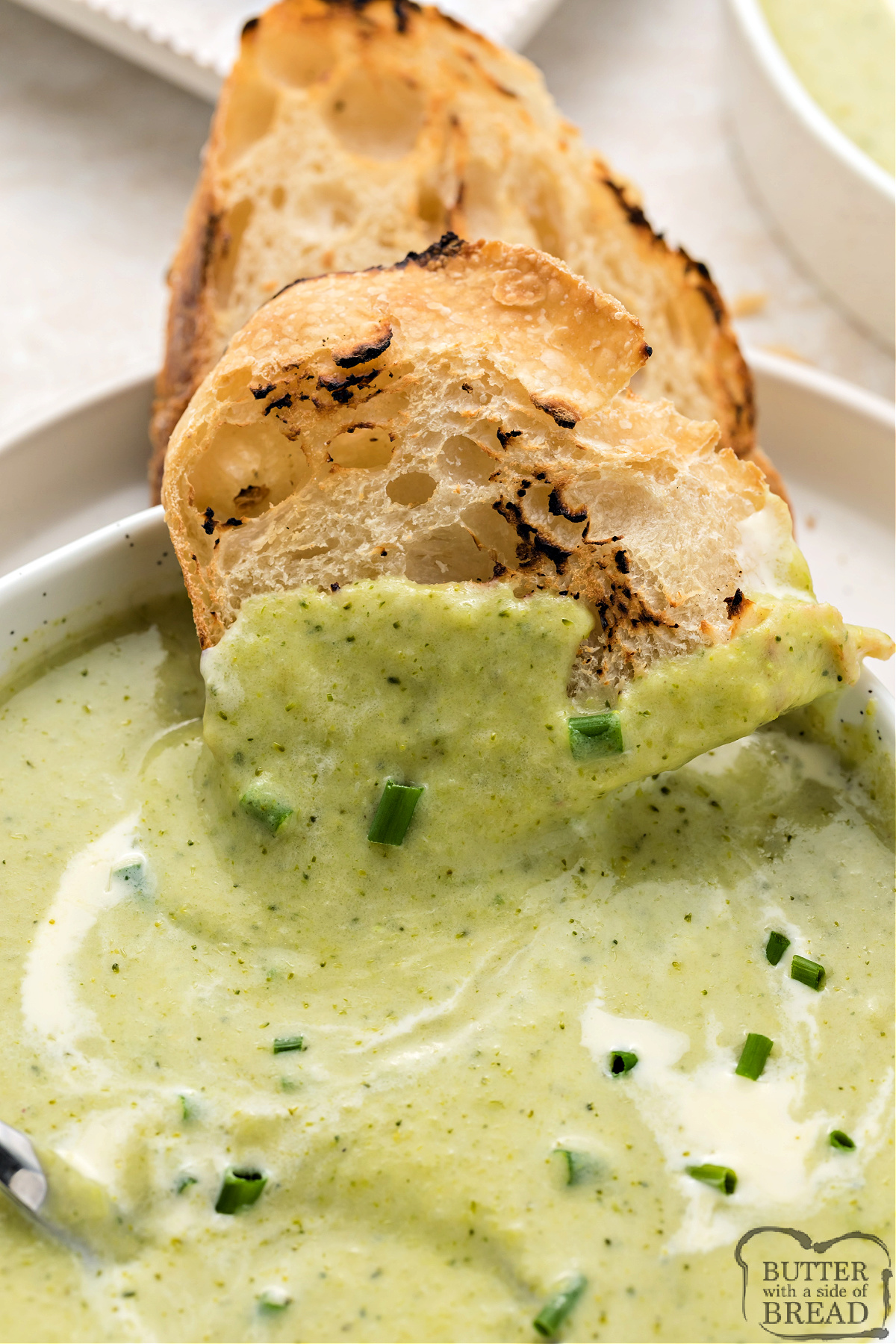Bowl of creamy broccoli soup garnished with fresh chives and served with crusty bread.