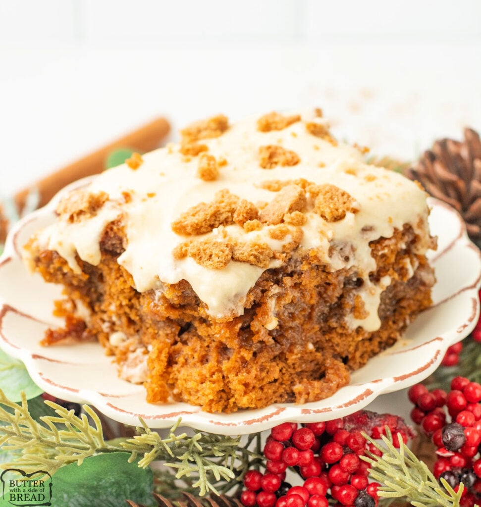 Slice of Gingerbread Poke Cake topped with fluffy molasses frosting and crushed gingerbread cookies on a white plate.
