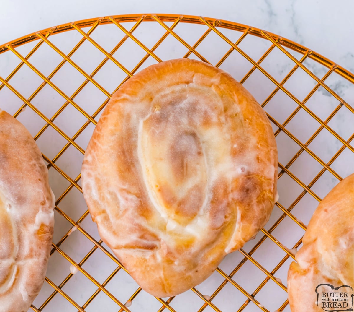 Homemade honey buns with a shiny glaze cooling on a wire rack.