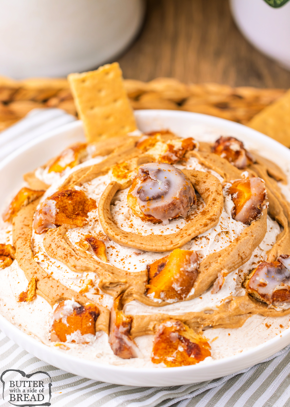 Bowl of creamy cinnamon roll dip topped with a cinnamon swirl and cinnamon roll pieces.