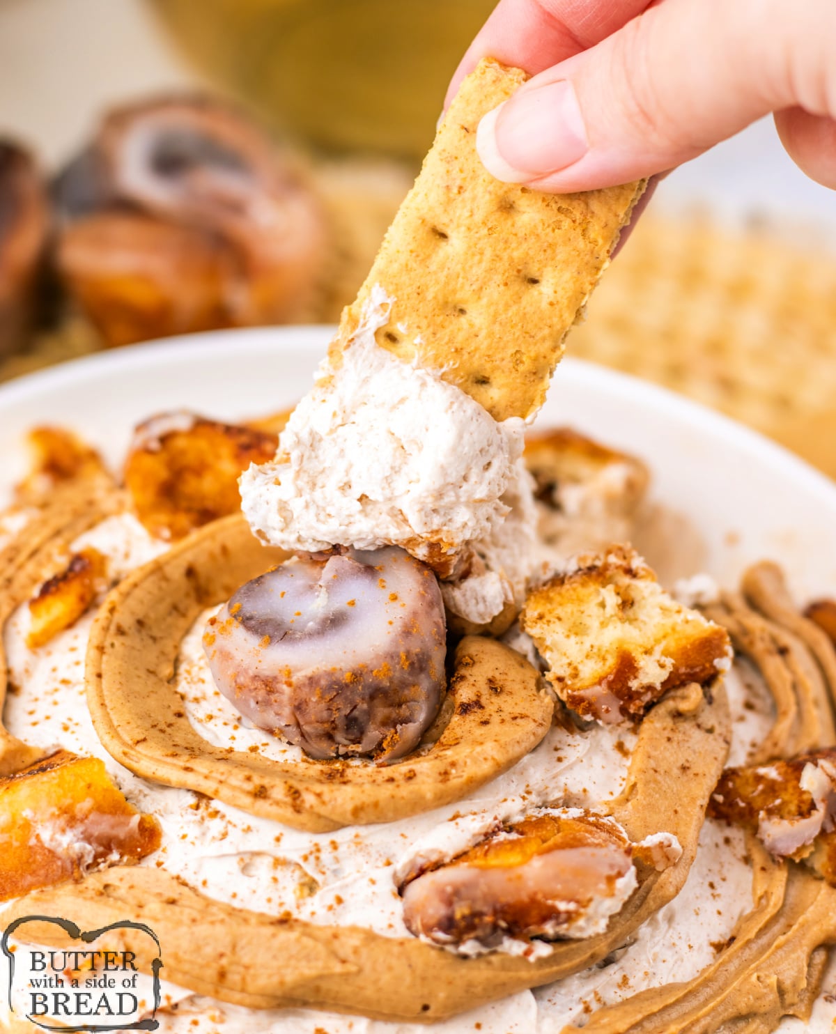 Close-up of cinnamon roll dip in a white bowl, decorated with a spiral cinnamon icing drizzle and small cinnamon roll pieces on top.