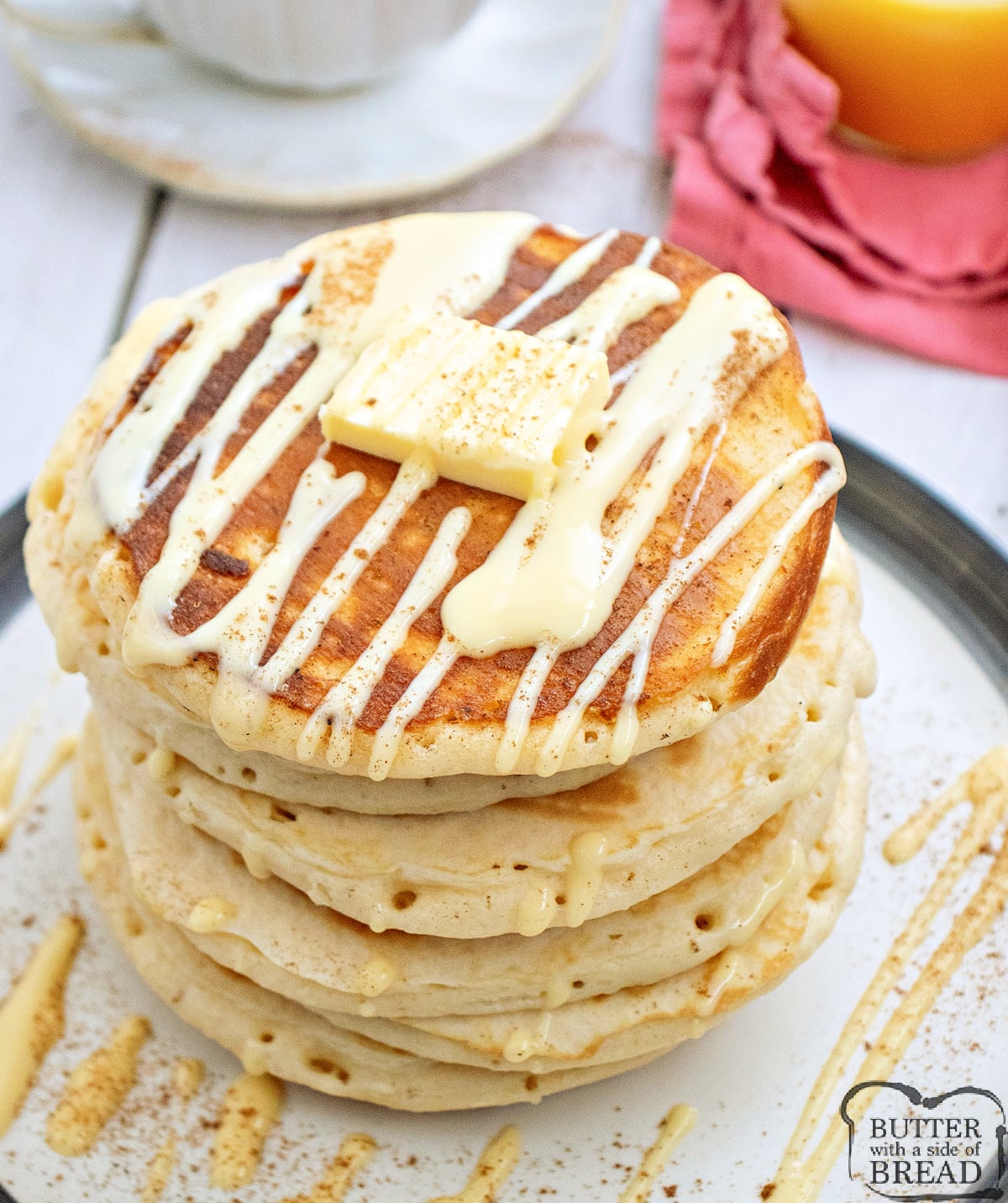 Stack of fluffy eggnog pancakes drizzled with eggnog glaze and topped with butter on a plate.