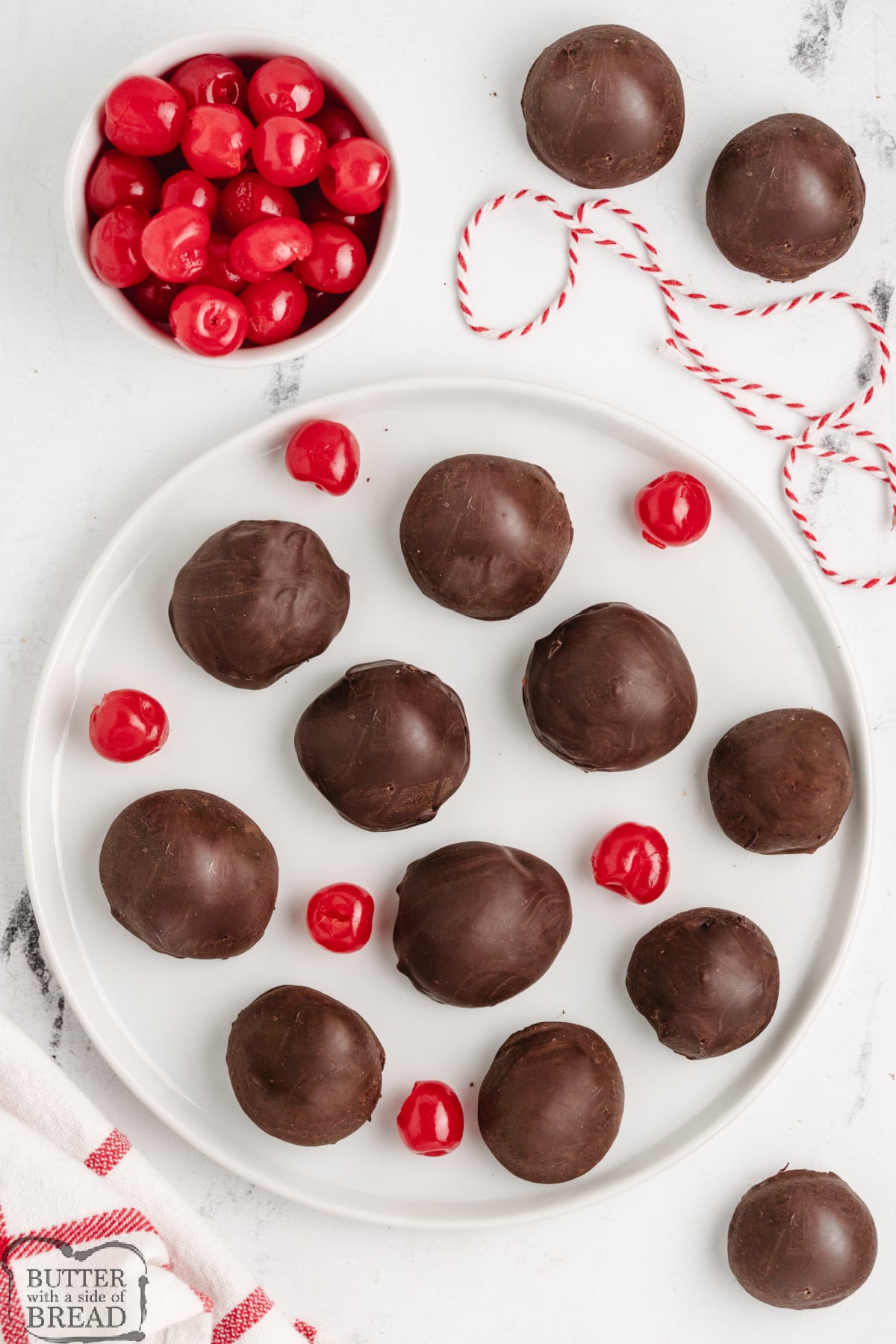 Overhead view of chocolate-covered cherries on a white plate.