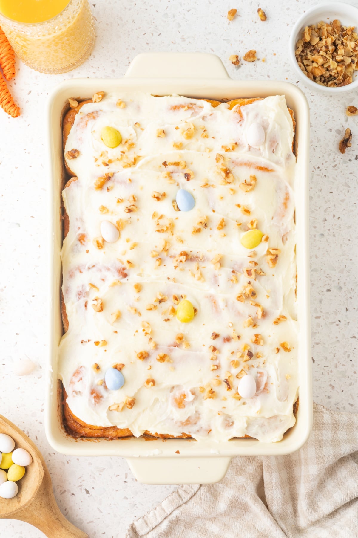 Carrot cake cinnamon rolls topped with cream cheese frosting and chopped walnuts in a baking dish.