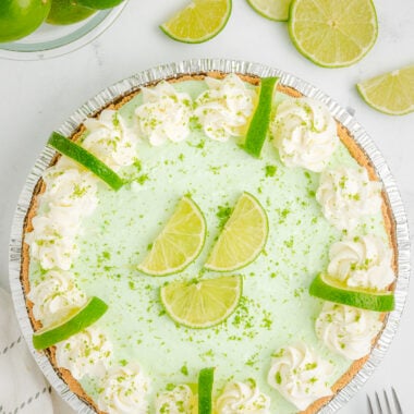 easy lime chiffon pie topped with whipped cream and sliced limes