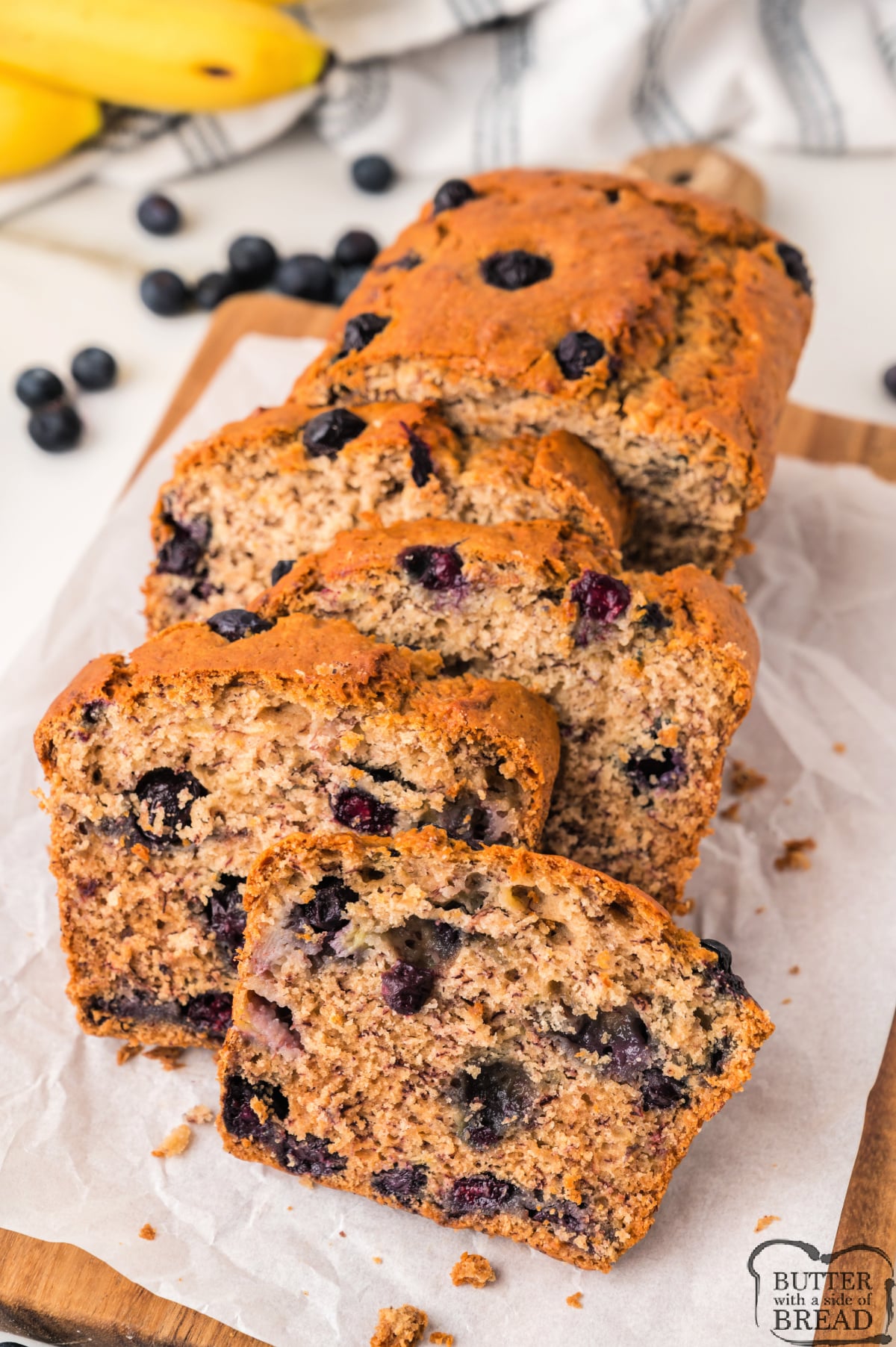 A close-up of moist blueberry banana bread with ripe bananas and fresh blueberries.