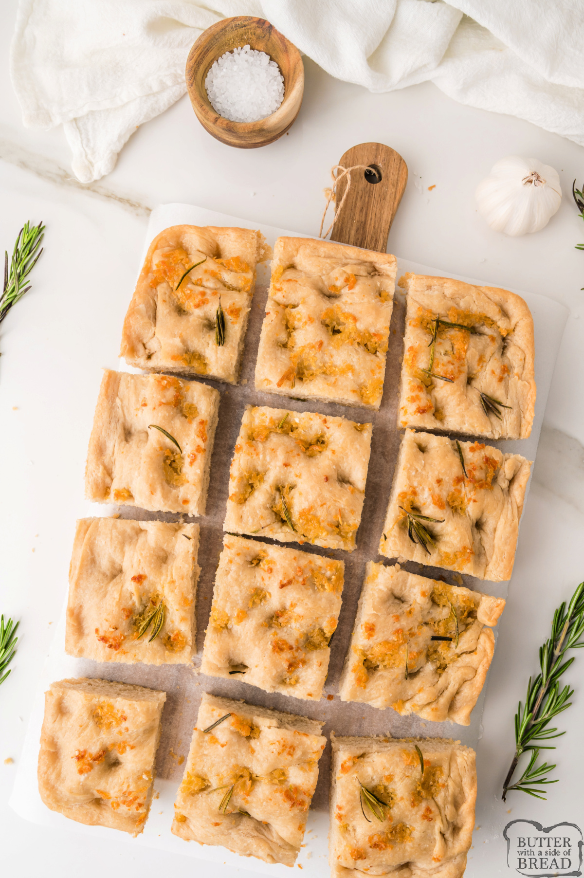 Sliced focaccia bread with golden crispy edges and a soft, fluffy center on a wooden cutting board.