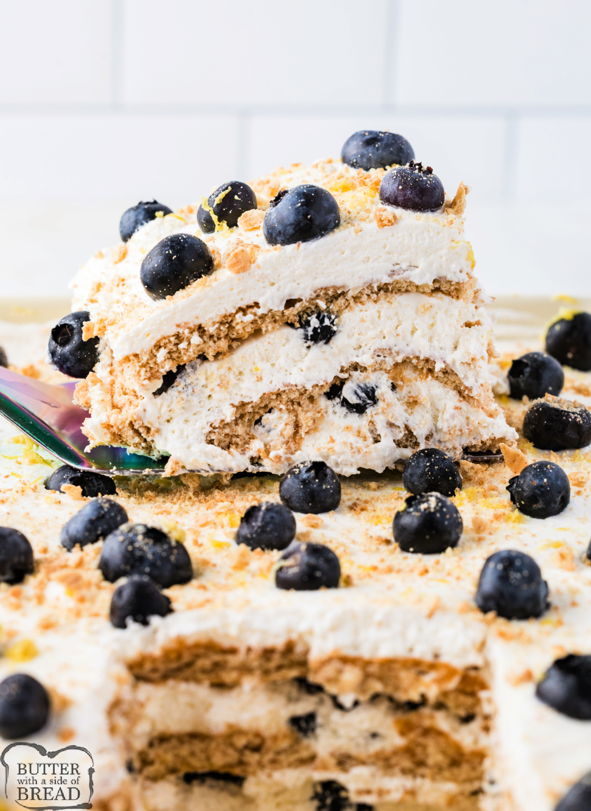 Three distinct layers of graham crackers, cream, and blueberries are visible in this slice of Lemon Blueberry Icebox Cake lifted from the pan.
