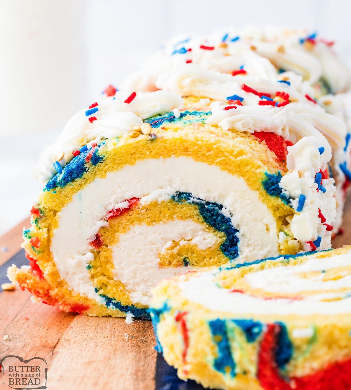 Patriotic cake roll on a serving board surrounded by red white and blue sprinkles for the 4th of July.
