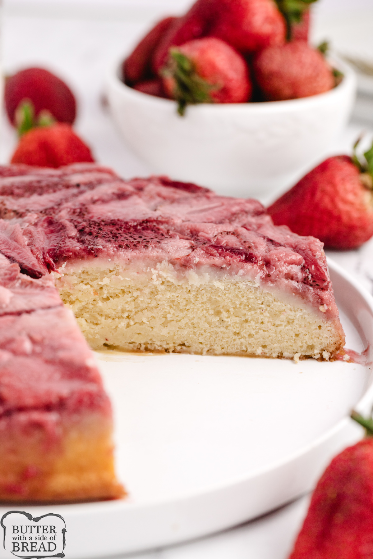 Strawberry upside-down cake just inverted onto a serving plate with juices dripping down the sides.
