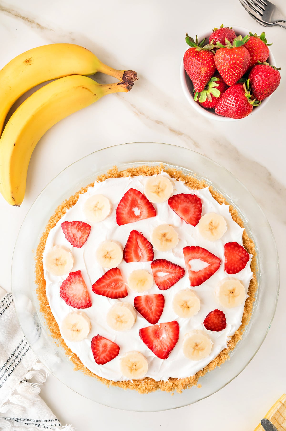 No bake strawberry banana pie in a pie dish with a vanilla wafer crust visible on the sides and fresh fruit on top.