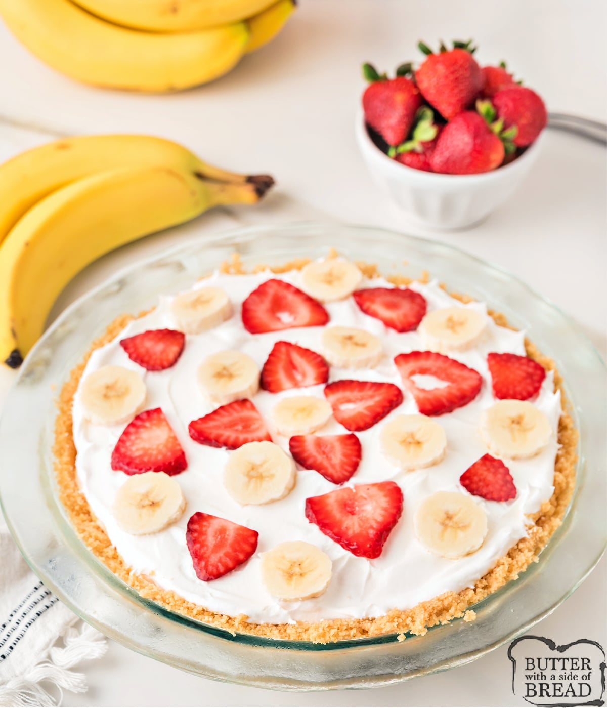 A no bake strawberry banana pie with a thick layer of cool whip and fresh fruit on top, ready to slice and serve.