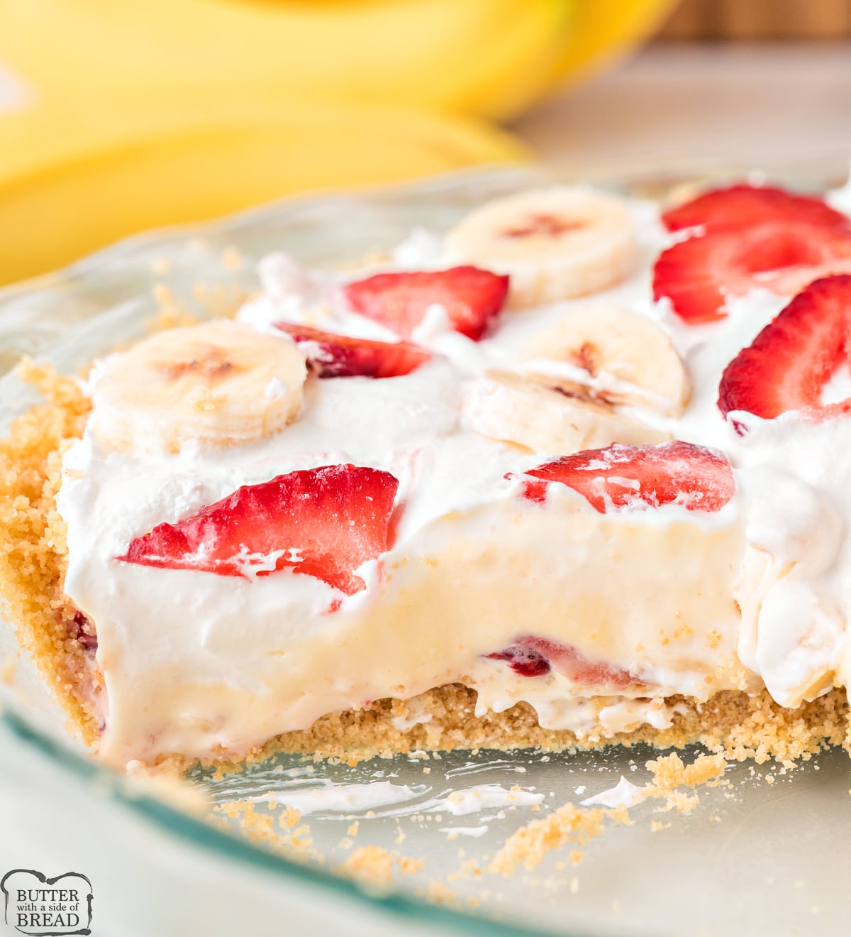 A whole no bake strawberry banana pie in a pie dish topped with cool whip, sliced strawberries, and banana slices.